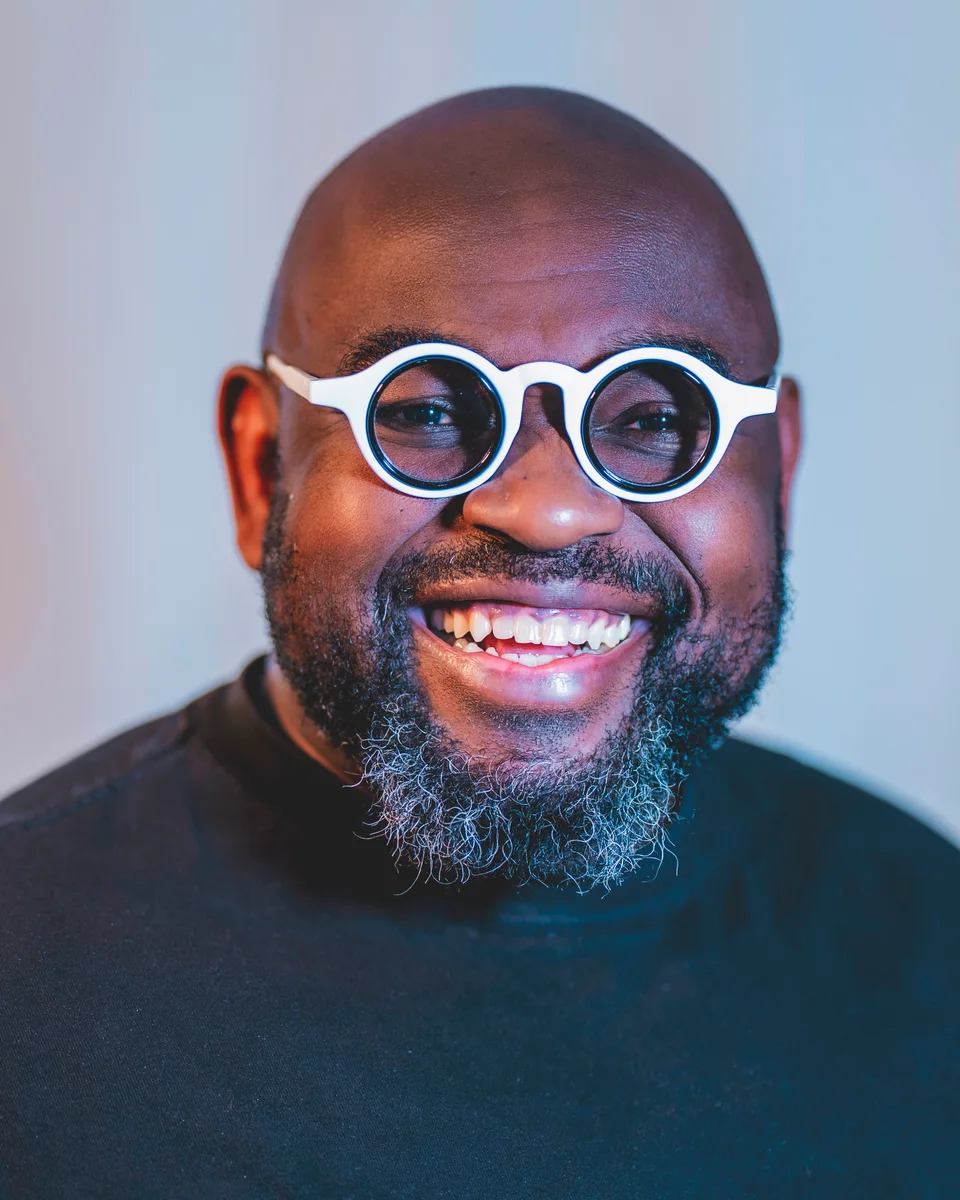 Portrait of Spencer Nugent, smiling, in round white-framed glasses